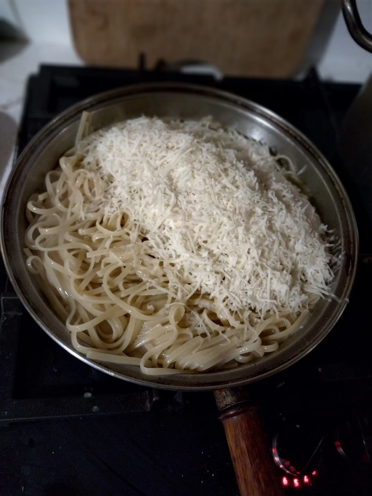 Finely grated pecorino Romano being added to linguine in the sauce pan