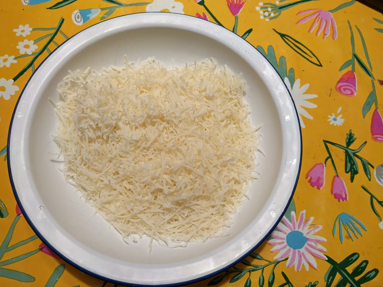 Finely grated pecorino Romano cheese in a white enamel bowl on a yellow floral cloth