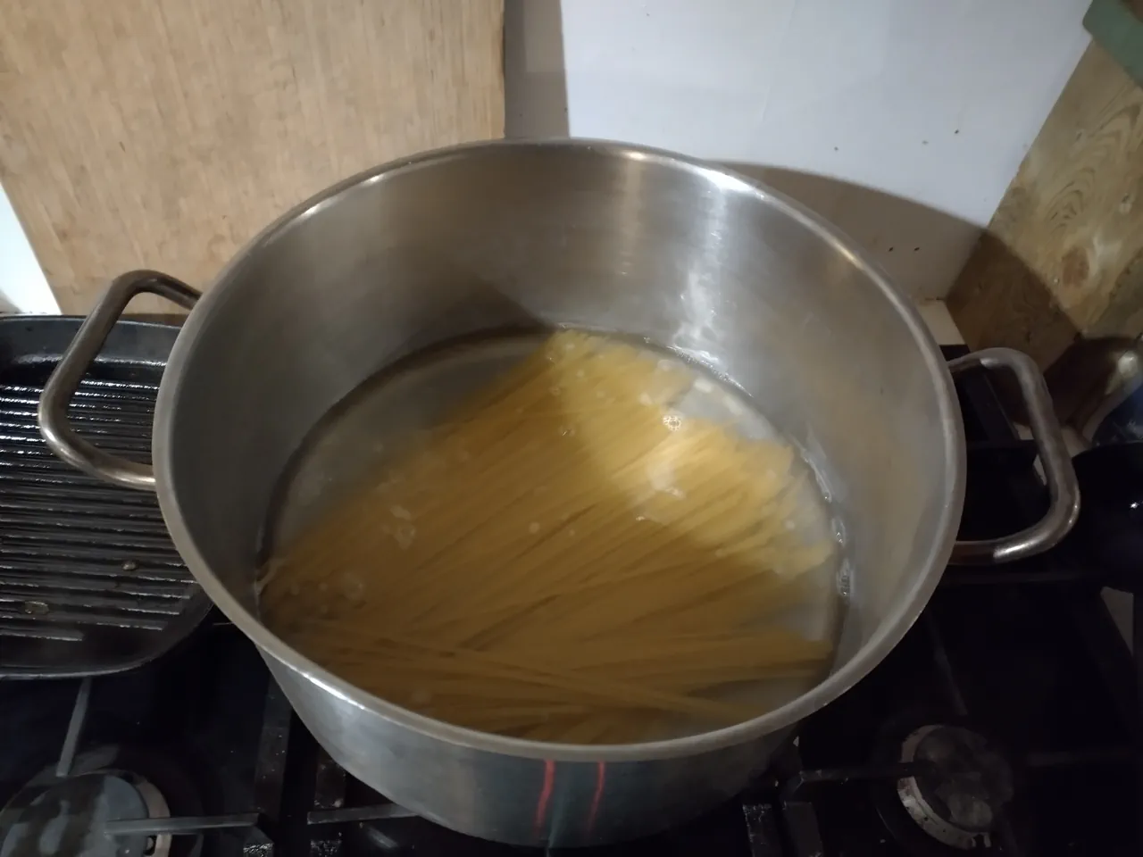 Linguine cooking in a wide saucepan with shallow starchy water for cacio e pepe