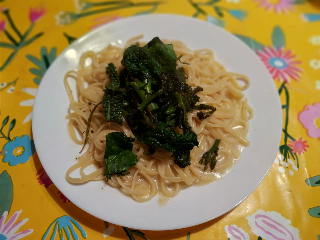 Cacio e pepe with charred winter greens served on a white plate on a yellow floral tablecloth