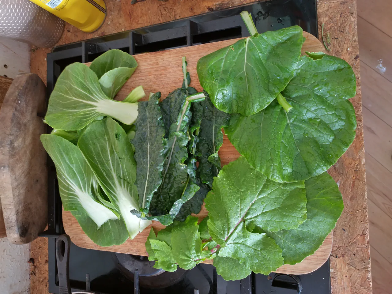 A wooden chopping board with freshly harvested pak choi, cavolo nero leaves, and mixed greens from the NFT hydroponic system