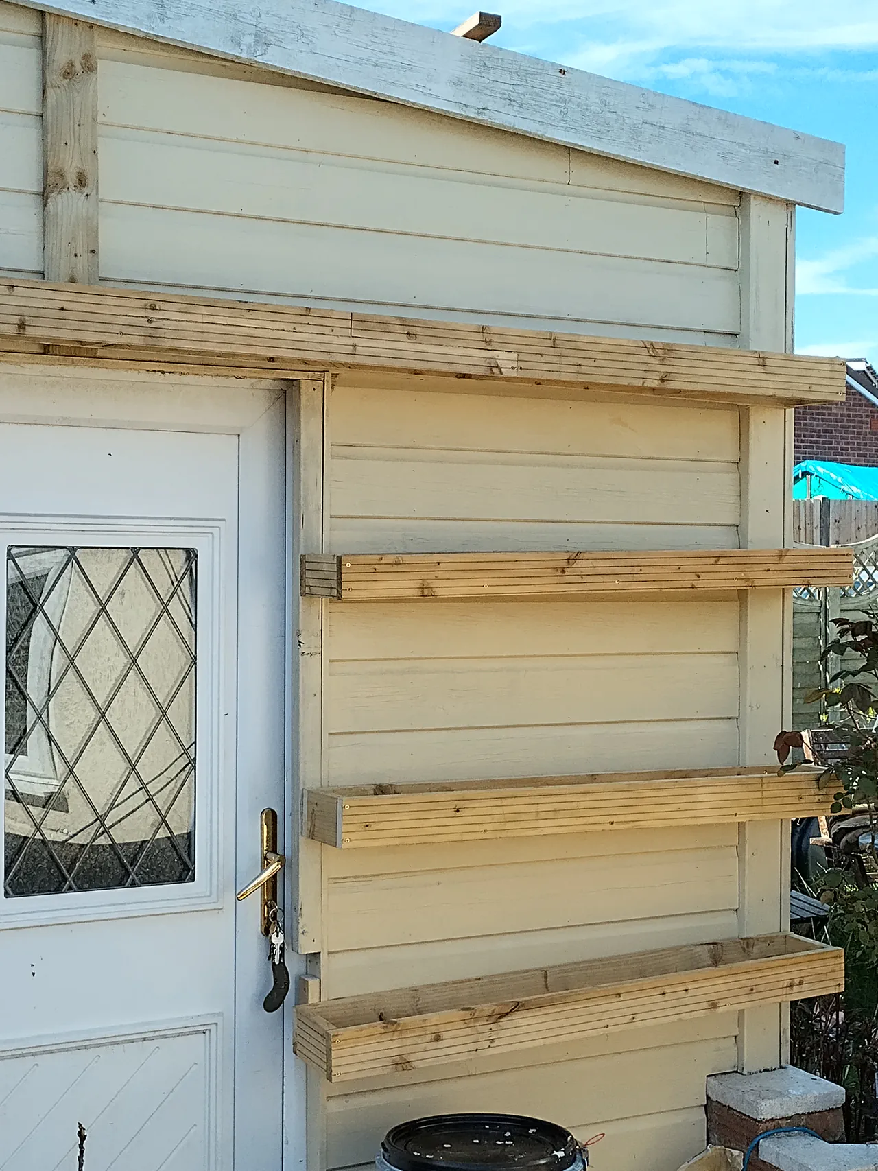 Three tiers of timber cradles mounted on the shed wall, empty, showing the clean construction with the longer top run extending past the door frame