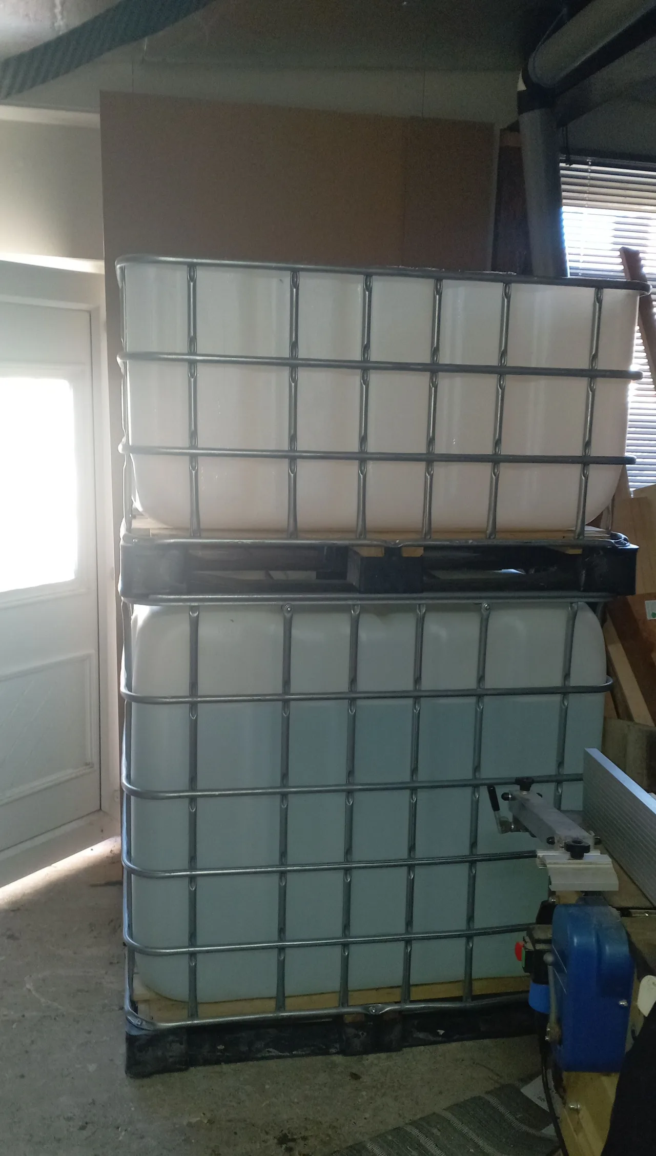 IBC tote tank cut and stacked in a workshop — the nutrient reservoir section sits on top of the full tank below, creating the height for gravity-fed nutrient delivery