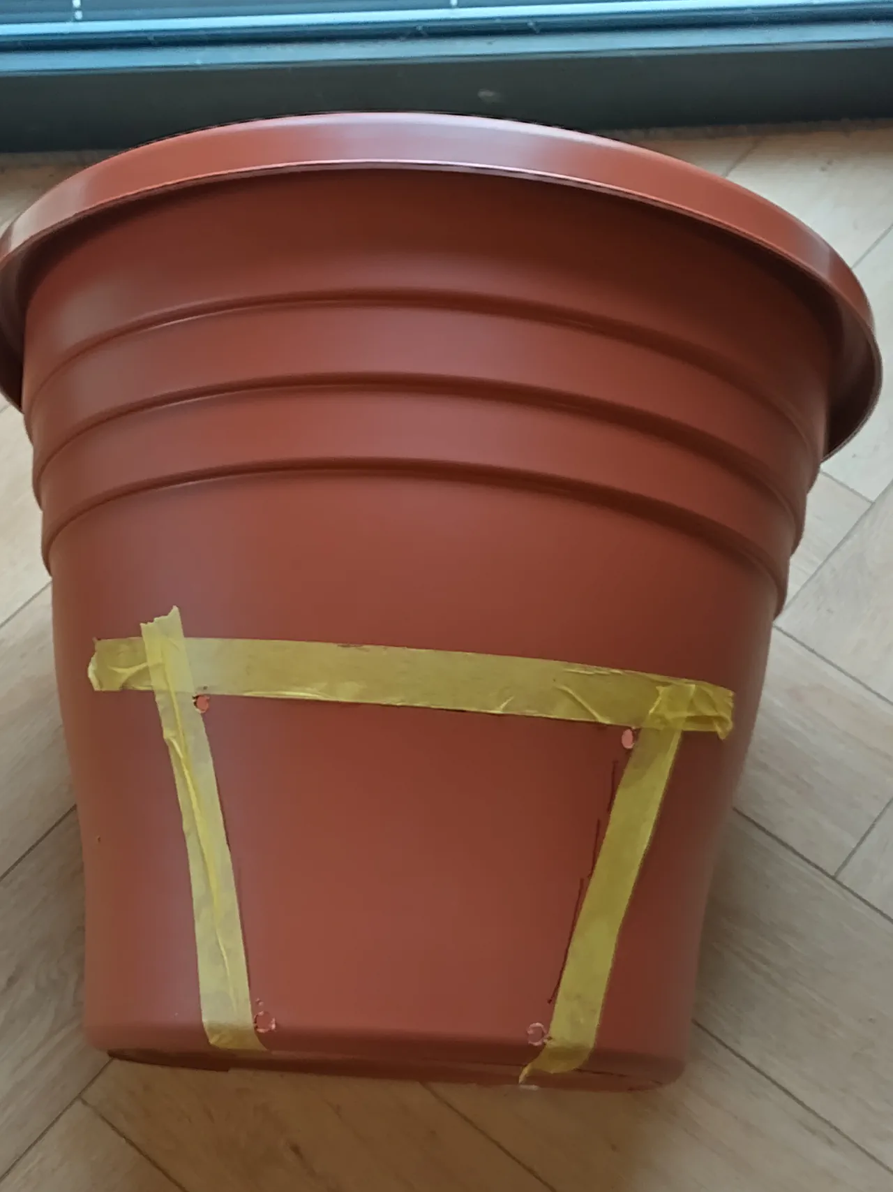 Side view of the pot showing masking tape guides and drilled corner holes ready for cutting